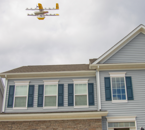 an image of a yellow and white Wing delivery drone flying over a house
